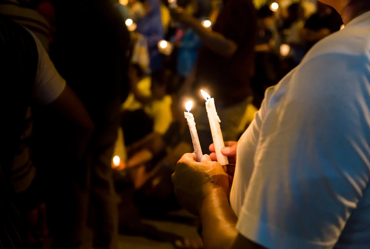 Side profile of someone holding candles amongst crowd. 