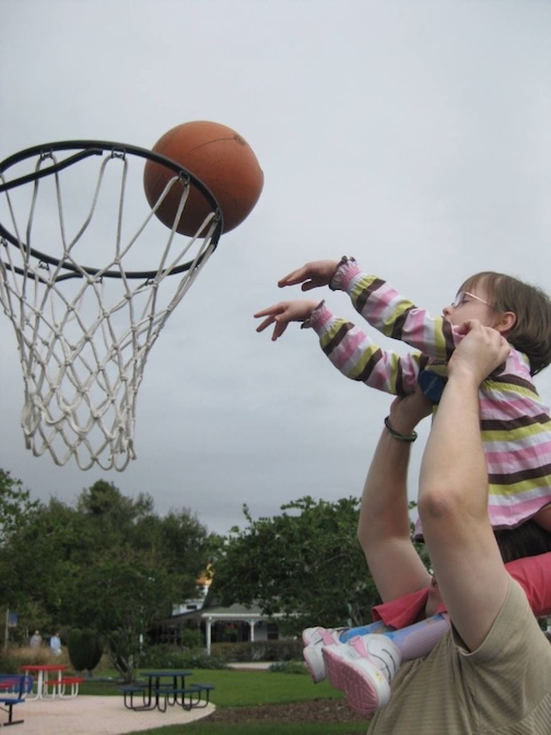 dad holding toddler daughter up to basket to dunk