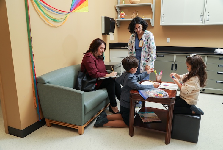 two children playing in a room with their mother in a room with a clinician.