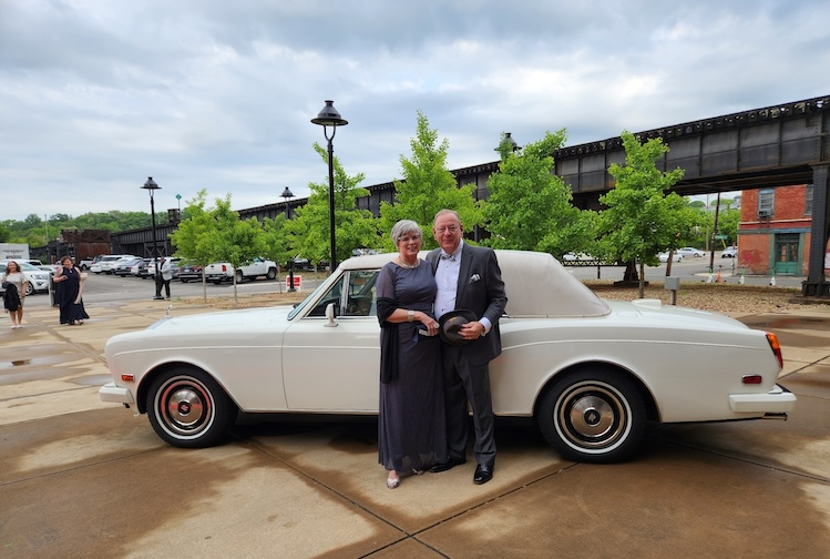 Man standing with woman next to an antique car, all dressed up for a gala