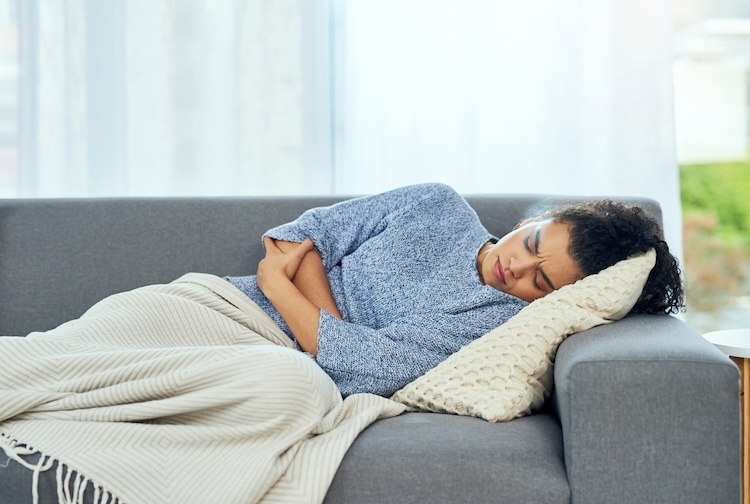 young woman experiencing stomach pain on the sofa at home