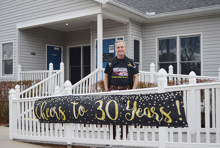 A doctor stands in front of a clinic with a banner that says,