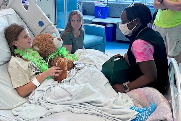 Jeniece Roane sits on a pediatric patient's bed and speaks with her and her parents.