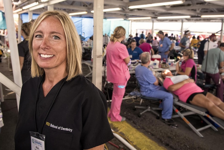 Blonde woman smiles while dentists are busy at work behind her taking care of patients